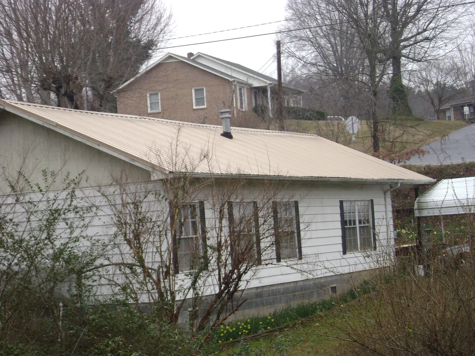 Tan metal roof on a white sided house set into a hillside — Commercial Roofing by Roofing Brothers in San Tan Valley
